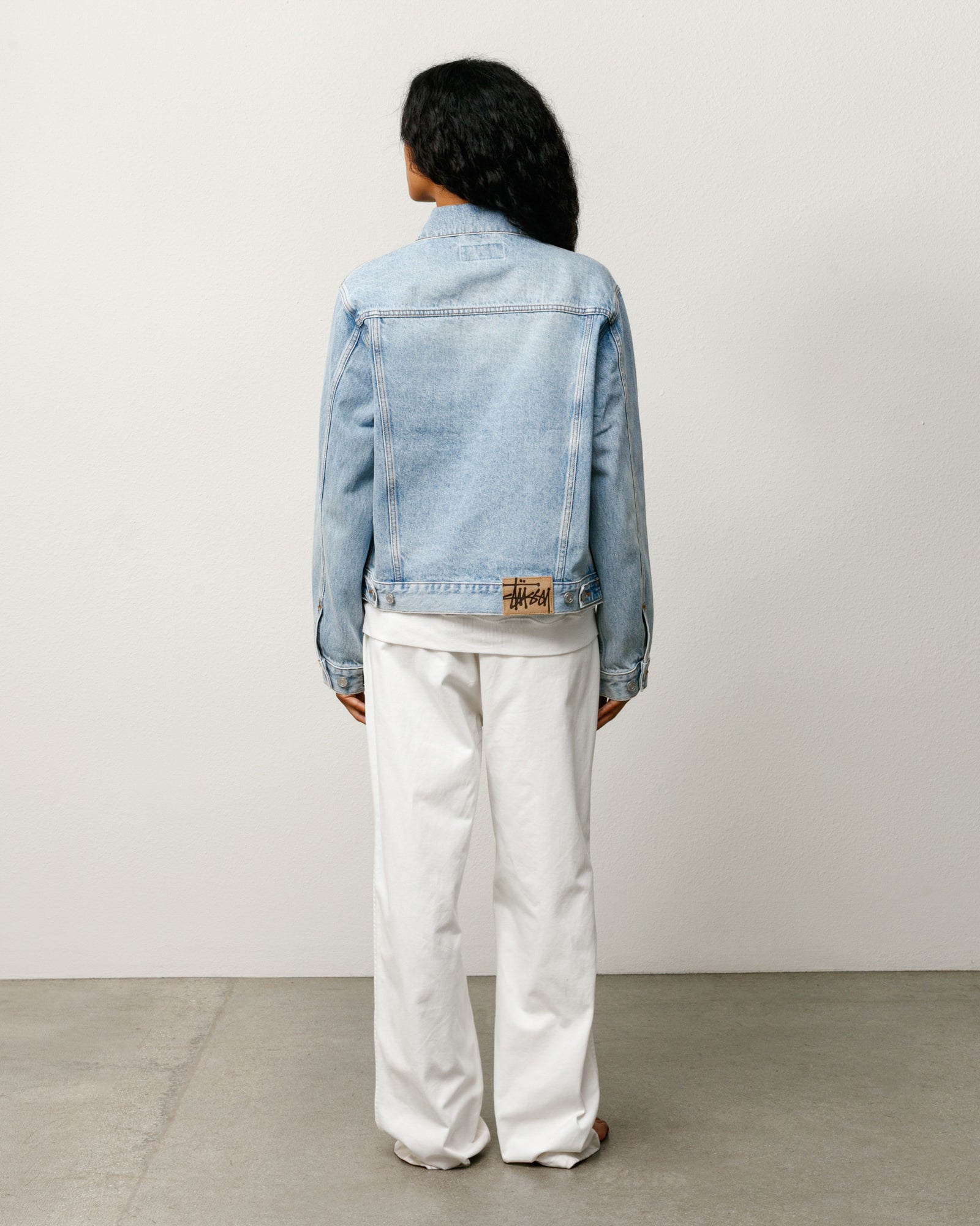 Unisex denim trucker jacket in light wash indigo, back view with suede Stüssy logo patch