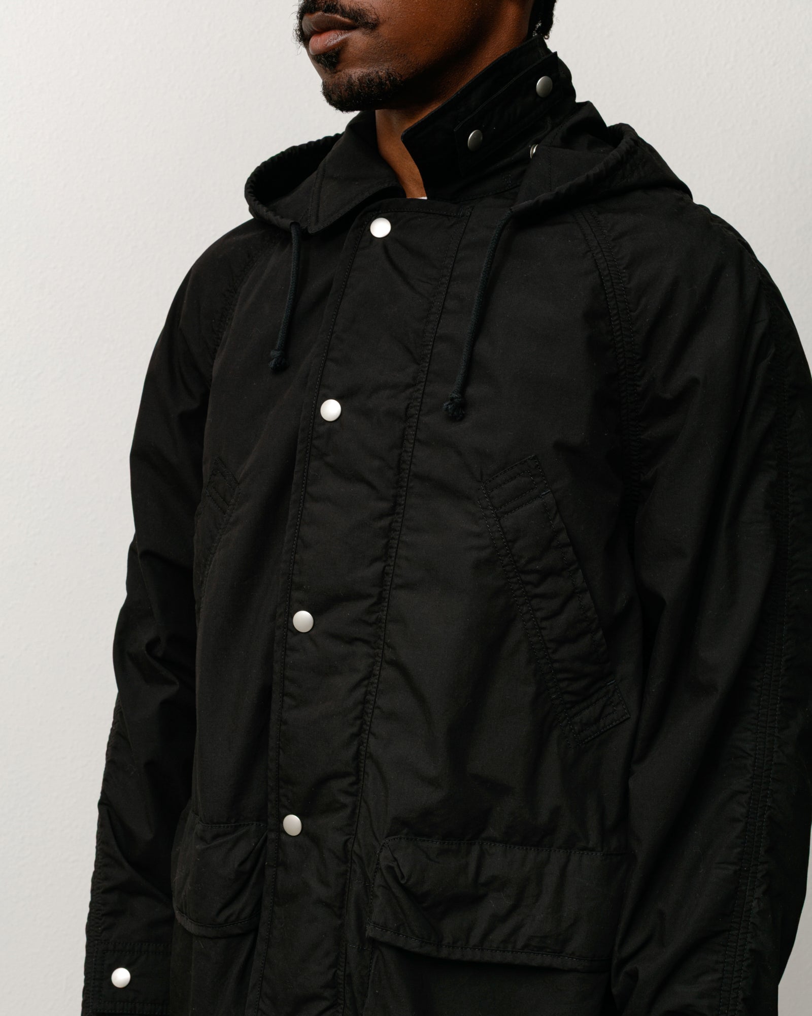 Lightweight field parka, unisex long-sleeve coat in black with snap placket and hood.