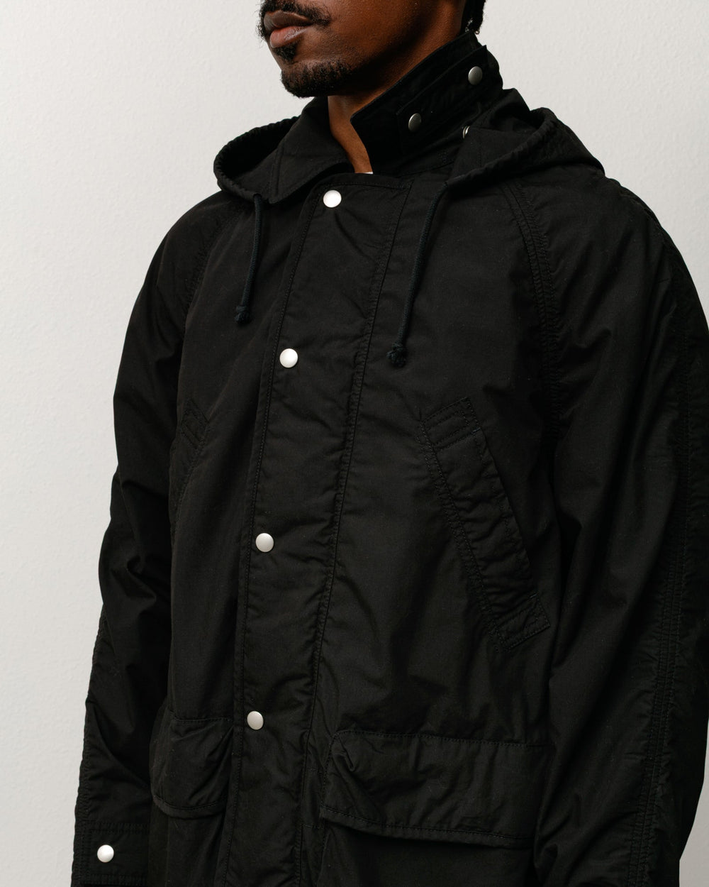 Lightweight field parka, unisex long-sleeve coat in black with snap placket and hood.